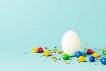 White Easter egg and multi-colored sweets on a blue background. Easter celebration concept