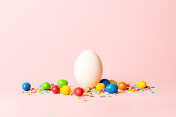White Easter egg and multi-colored sweets on a pink background. Easter celebration concept