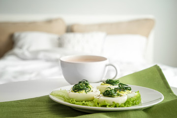 Plate with tasty deviled eggs and cup of coffee on bed