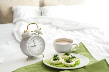 Plate with tasty deviled eggs and cup of coffee on bed