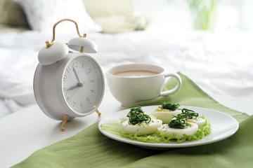 Plate with tasty deviled eggs and cup of coffee on bed