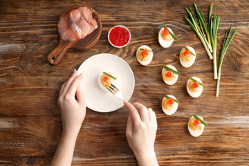 Woman eating tasty deviled eggs on wooden table