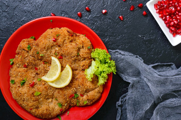 Large Viennese schnitzel on a red plate with lemon on a black background. Meat dish. Top view, flat...