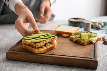 Woman preparing tasty sandwich with avocado in kitchen, closeup
