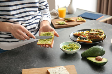 Woman preparing tasty sandwich with avocado in kitchen