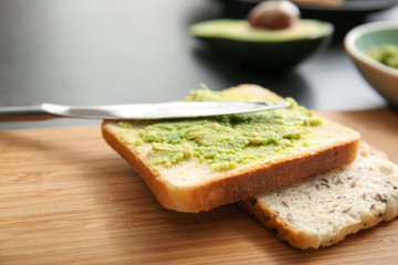 Tasty bread with mashed avocado and knife on wooden board, closeup