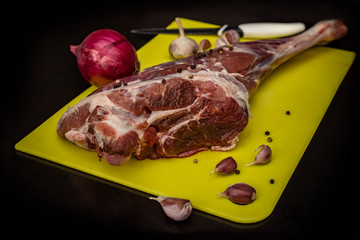Raw meat, leg of lamb on a cutting board of bright color with onions and garlic, on a dark background. Copy space