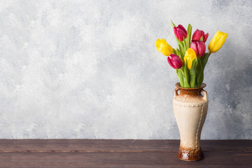 Bouquet of yellow and pink tulips in vase on a gray background. Copy space for product and text.