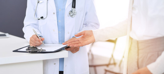 Unknown woman doctor and  female patient  discussing something while standing near reception desk in emergency hospital. Physician at work in clinic. Medicine and health care concept