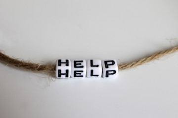 A cube with the HELP alphabet connected by a rope to a white background.