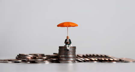 Stack of coins and a miniature people with a orange umbrella.