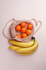 fruits tangerine, banana in recycling net market bag on white background. String mesh bag, minial concept, recycle idea
