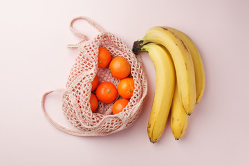 fruits tangerine, banana in recycling net market bag on white background. String mesh bag, minial concept, recycle idea