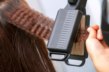 Close up of stylist hands with styling iron straightening woman hair at salon