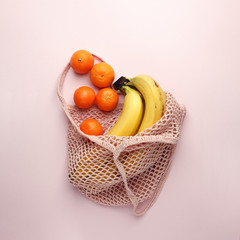 Mesh shopping bag with exotic fruits on pink canvas background. Summer time blogger organic food concept, minimal