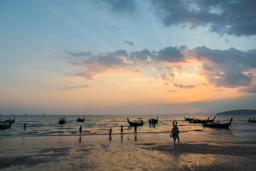 Beautiful sunset on a beach in Thailand with people and local boats