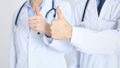 Team of unknown medicine doctors showing OK sign with thumb up close up. Success and high level service in health care, best treatment and customer loyalty and physical concept