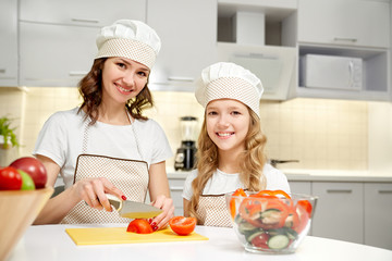 Mother and daughter posing in kitchen, cooking salad.