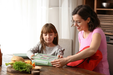 Mother with cute daughter preparing school lunch at home