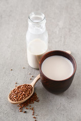 Cup and bottle of tasty buckwheat milk on grey table