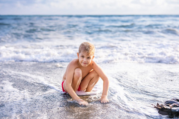 Child boy playing in the waves on the beach in summer sunset, kid watching sea waves and having fun