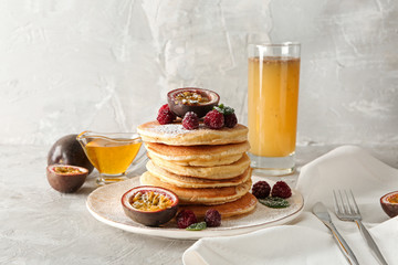 Tasty pancakes with passion fruit and berries on grey table