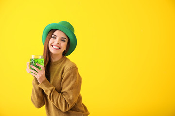 Beautiful young woman in green hat and with mug of beer on color background. St. Patrick's Day...