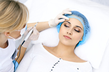 Professional beautician doing eyebrow tattoo at woman face. Permanent brow makeup in beauty salon, closeup.  Cosmetology treatment