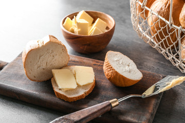 Board with cut fresh bread and butter on grey table