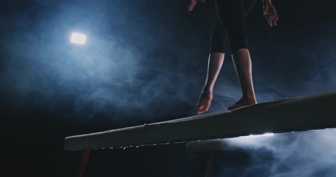 Close-up of the foot of a professional gymnast girl jumping in slow motion in the smoke on a balance beam. Women's gymnastics. Grace and a healthy lifestyle