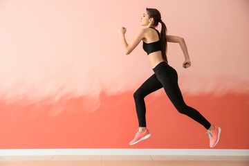 Sporty young woman running against color wall