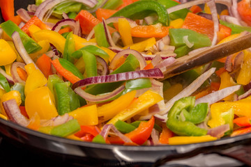 Close up of green peppers, yellow peppers, red peppers and red onion being cooked in a non-stick pan