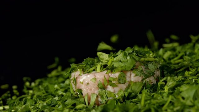 Raw pork meat with chopped parsley on black background in slowmotion.