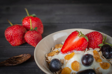 Yoghurt mix oatmeal, strawberry and grape topping in white bowl on the wood table with spoon and strawberries placed beside.