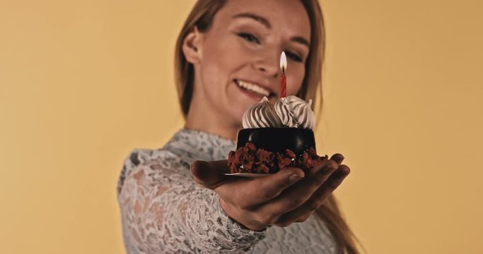 Woamn is holding birthday cake with one candle on orange background.