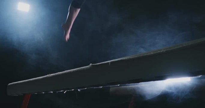 Legs Professional girl gymnasts jump in slow motion in the smoke on the balance beam. Women's Artistic Gymnastics