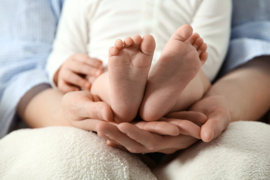 Mother holding feet of her cute little baby at home