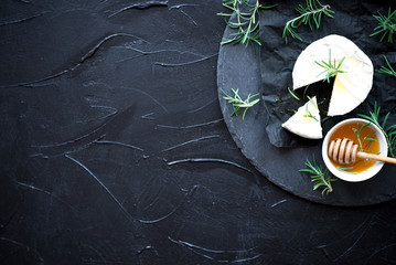 Brie type of cheese.Сamembert cheese with rosemary and honey on black slate background.Italian,...