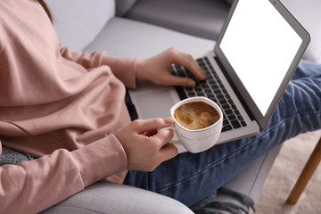 Young woman working on laptop and drinking coffee at home