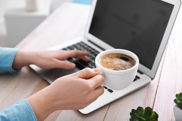 Young woman working on laptop and drinking coffee at table
