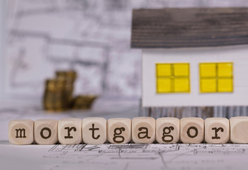 Word MORTGAGOR composed of wooden letter. Small paper house in the background.
