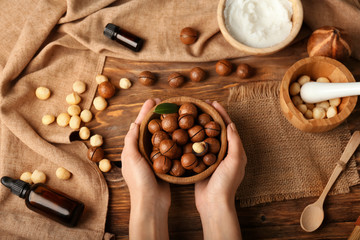 Female hands with macadamia nuts and natural cosmetics on wooden background