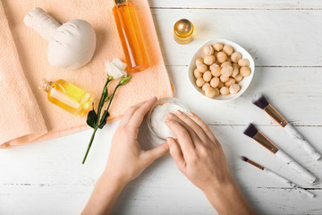 Female hands using flesh of macadamia nuts for skin on wooden background