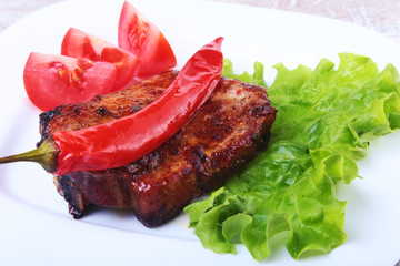 Beef steak on barbeque and chili pepper with tomato, lettuce leaves on white plate