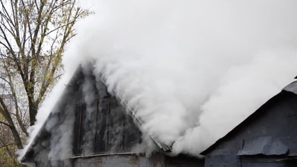 White thick smoke comes from the burning roof of the house