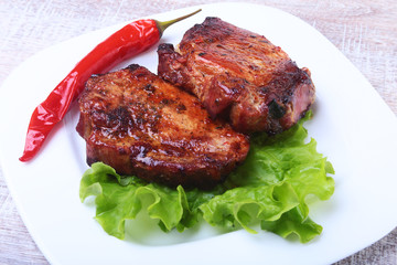 Beef steak on barbeque and chili pepper with tomato, lettuce leaves on white plate