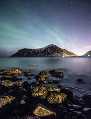 Aurora borealis with stars over mountain with rock on coastline