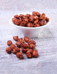 Sugared Hazelnuts in a white bowl on a wooden background. Hazelnuts in sugar glaze. Selective focus.