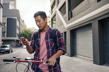 Fototapeta na wymiar Young Asian man walking with his bike using a cellphone