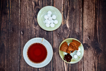 Cup of tea, chocolate, cranberry in sugar and cookies on the saucers. All on the wood boards. Top view, flat lay